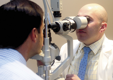 Doctor examining patient eyes through optometry machine lenses.
