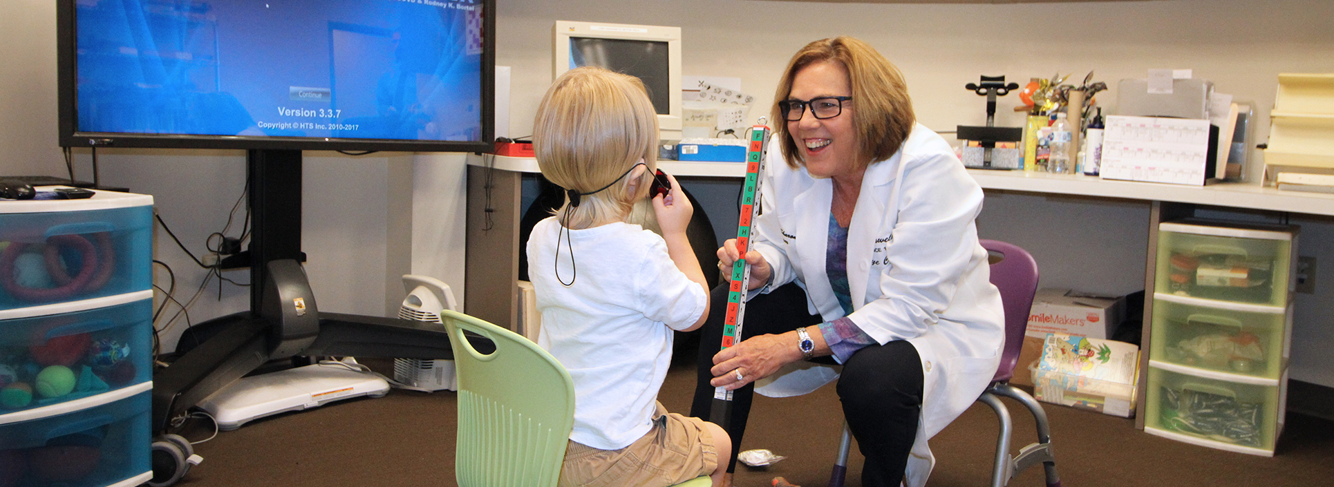Dr. Sharon Berger smiling and holding a multicolored stick with a young boy holding an eye patch during a vision therapy session.