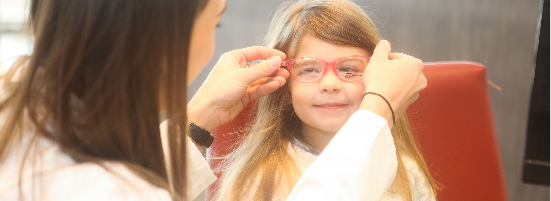 An employee of Roswell Eye Clinic placing a pair of glasses on young girl's smiling face.