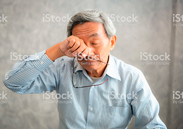 Asian man rubbing his eyes, holding his glasses.