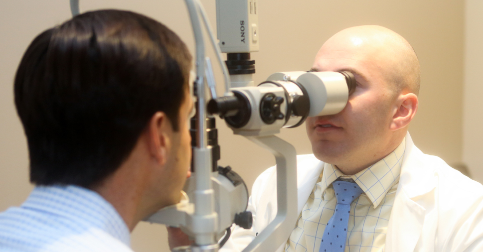 Dr. Scott Moscow using eye equipment to examine the eyes of a male.