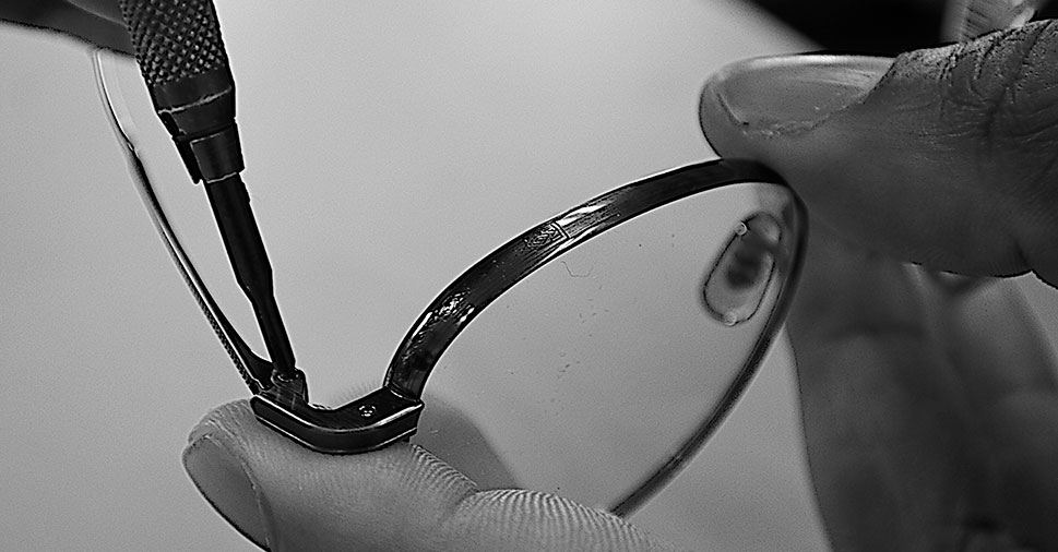 Hands holding the frames of a pair of glasses while someone is screwing in a scew on the side of the glasses.