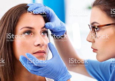 A lady nurse, wearing gloves, examining the eyes of a female patient.