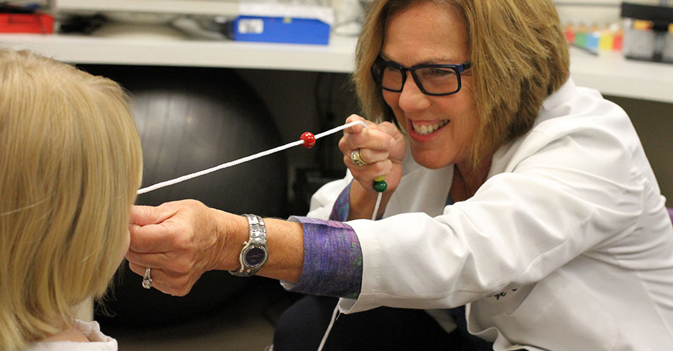 Smiling Dr. Sharon Berger of the Roswell Eye Clinic holding a string up to a young boy's face during a vision therapy session.