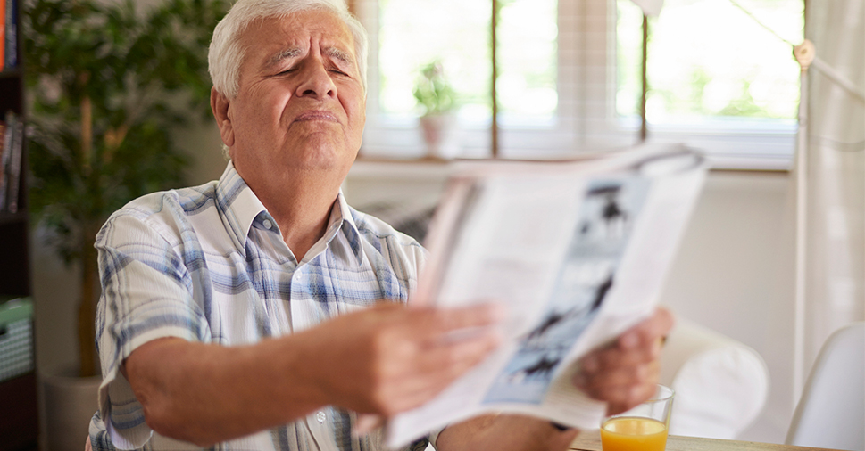 Man with poor eye sight holding newspaper squinting.