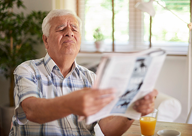 Man with poor eye sight holding newspaper squinting.